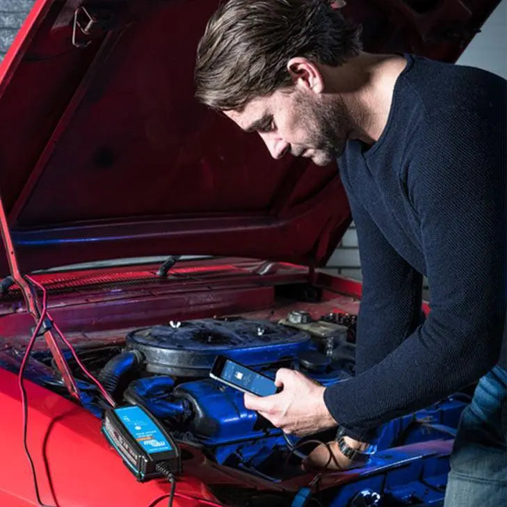 Man inspecting red car engine with Blue Smart charger device connected to blue engine components.